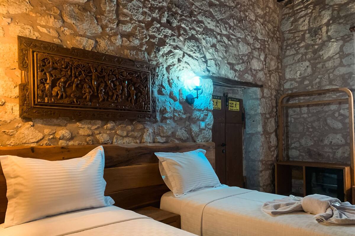A room with two beds, stone walls, a wooden headboard, a wall-mounted light, and a sign indicating a low-light area.