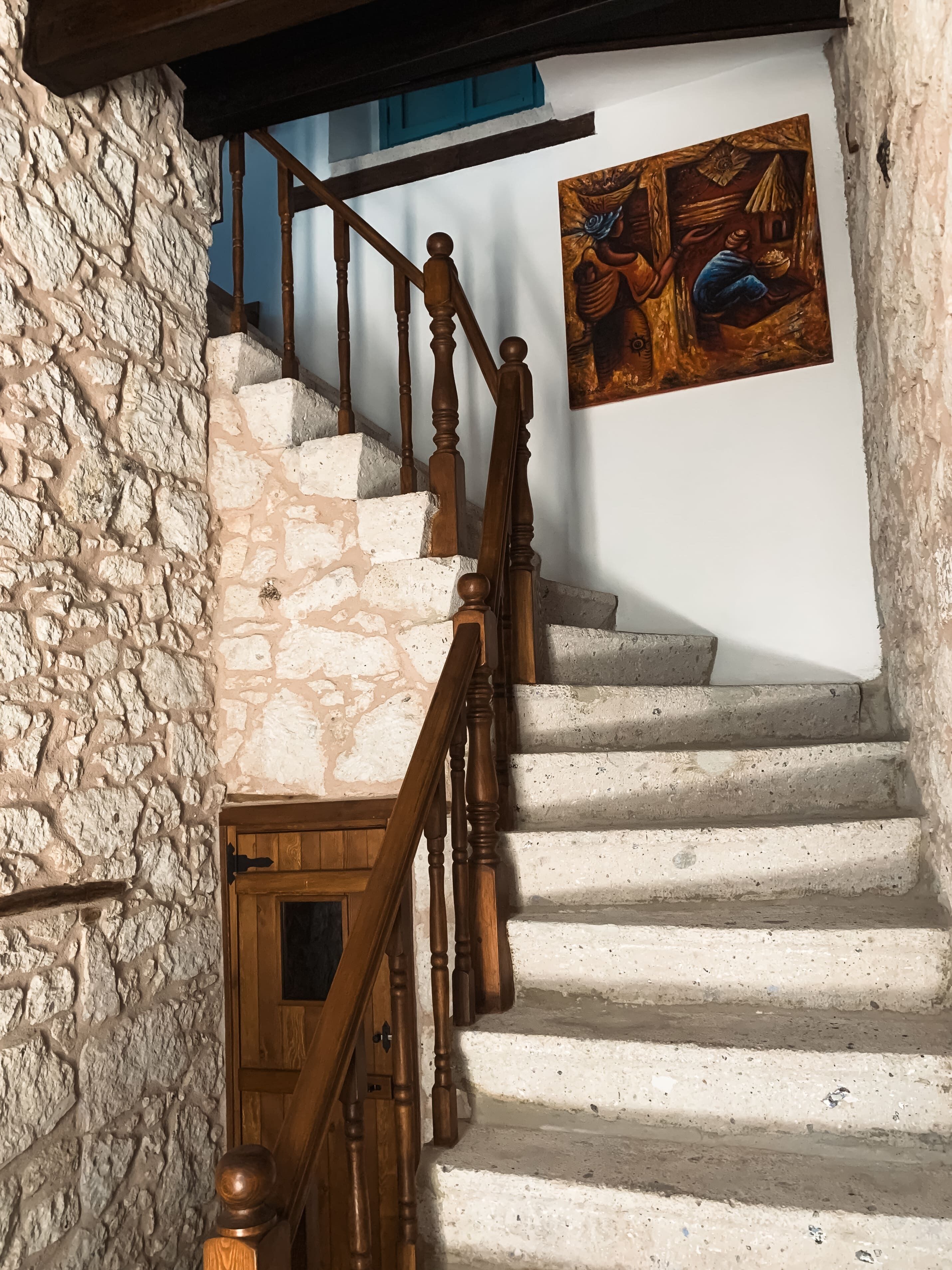 A staircase with stone walls and wooden balusters, leading to a room with a painting on the wall.