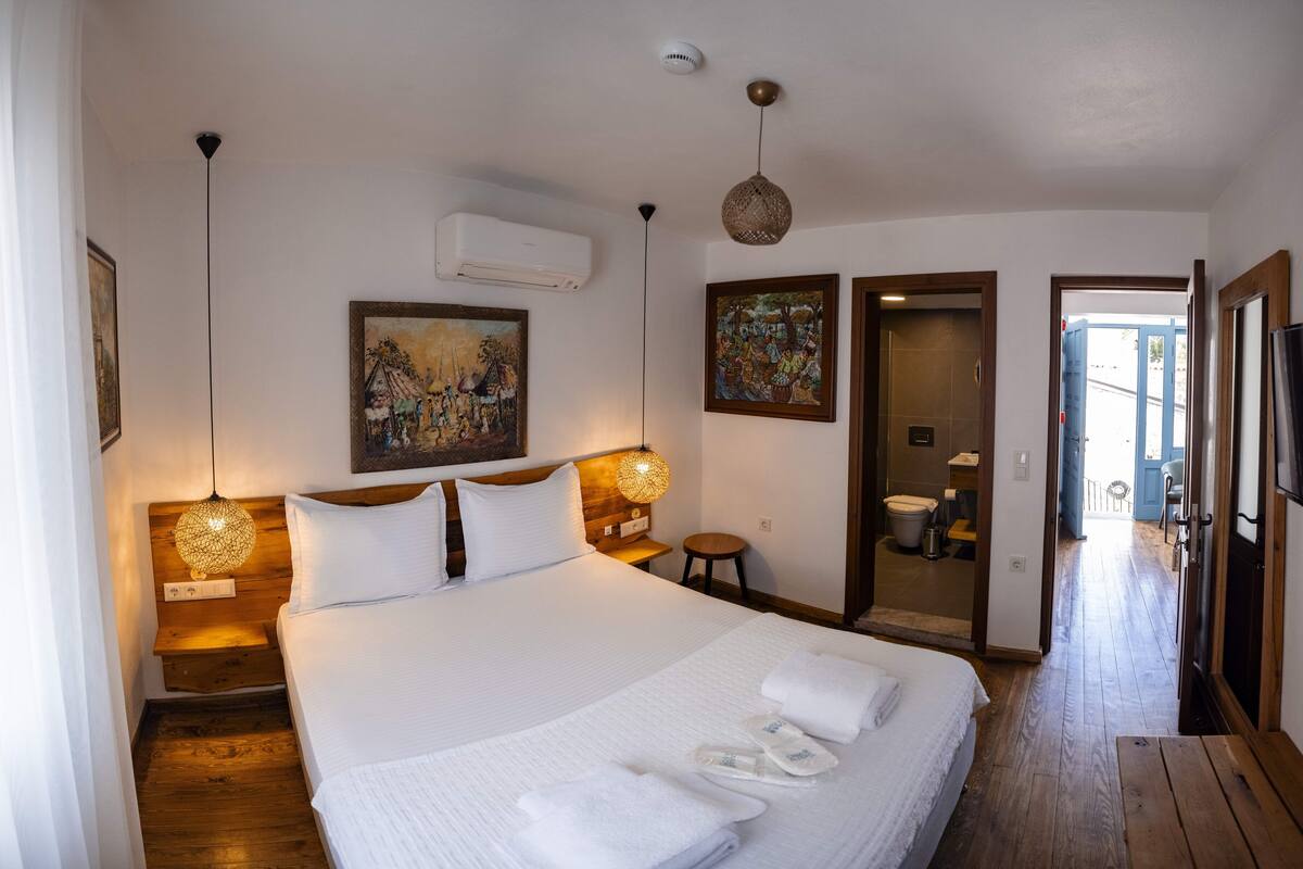 A neatly made bed with white linens and towels, a wooden headboard, and two wall-mounted lamps.