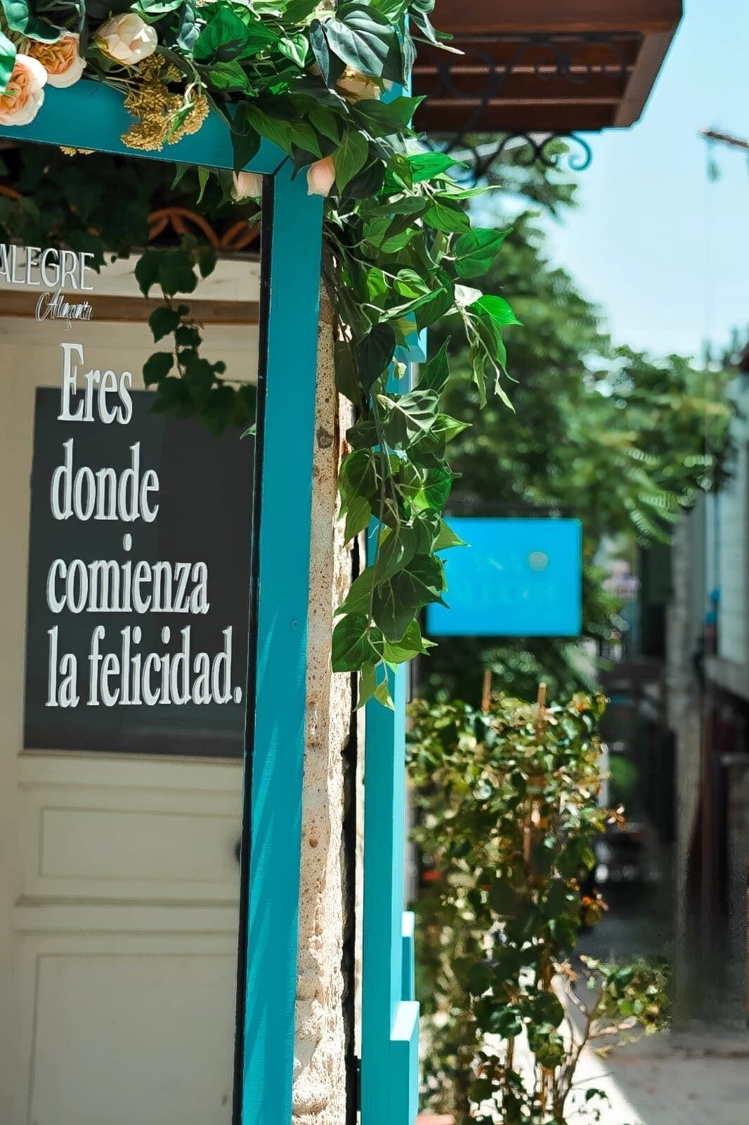 Un letrero con un mensaje en español, una estructura color turquesa y follaje verde.