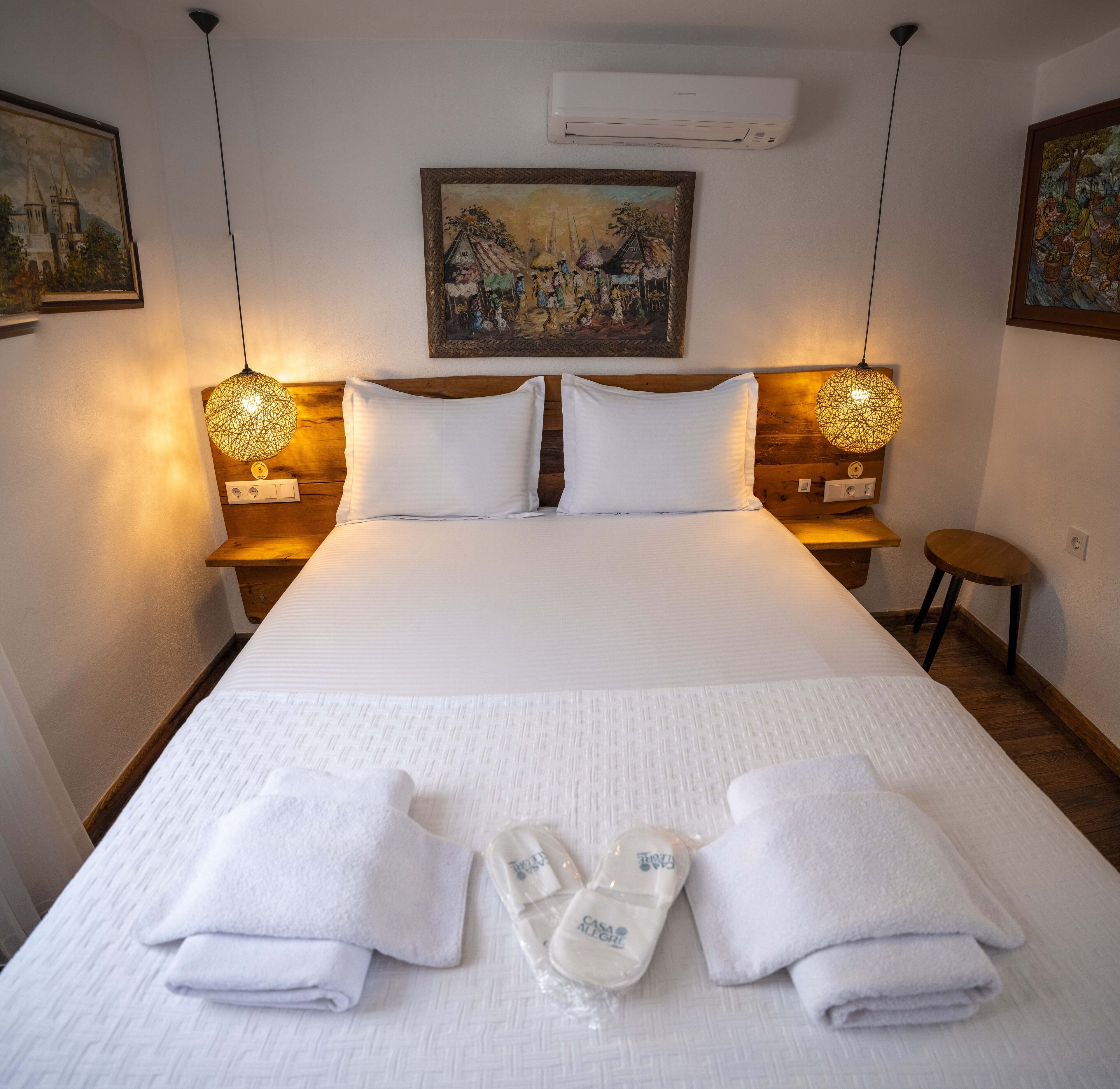 Ein Hotelzimmer mit einem großen Bett, zwei Nachttischen, einem Wandbild und einer Klimaanlage.