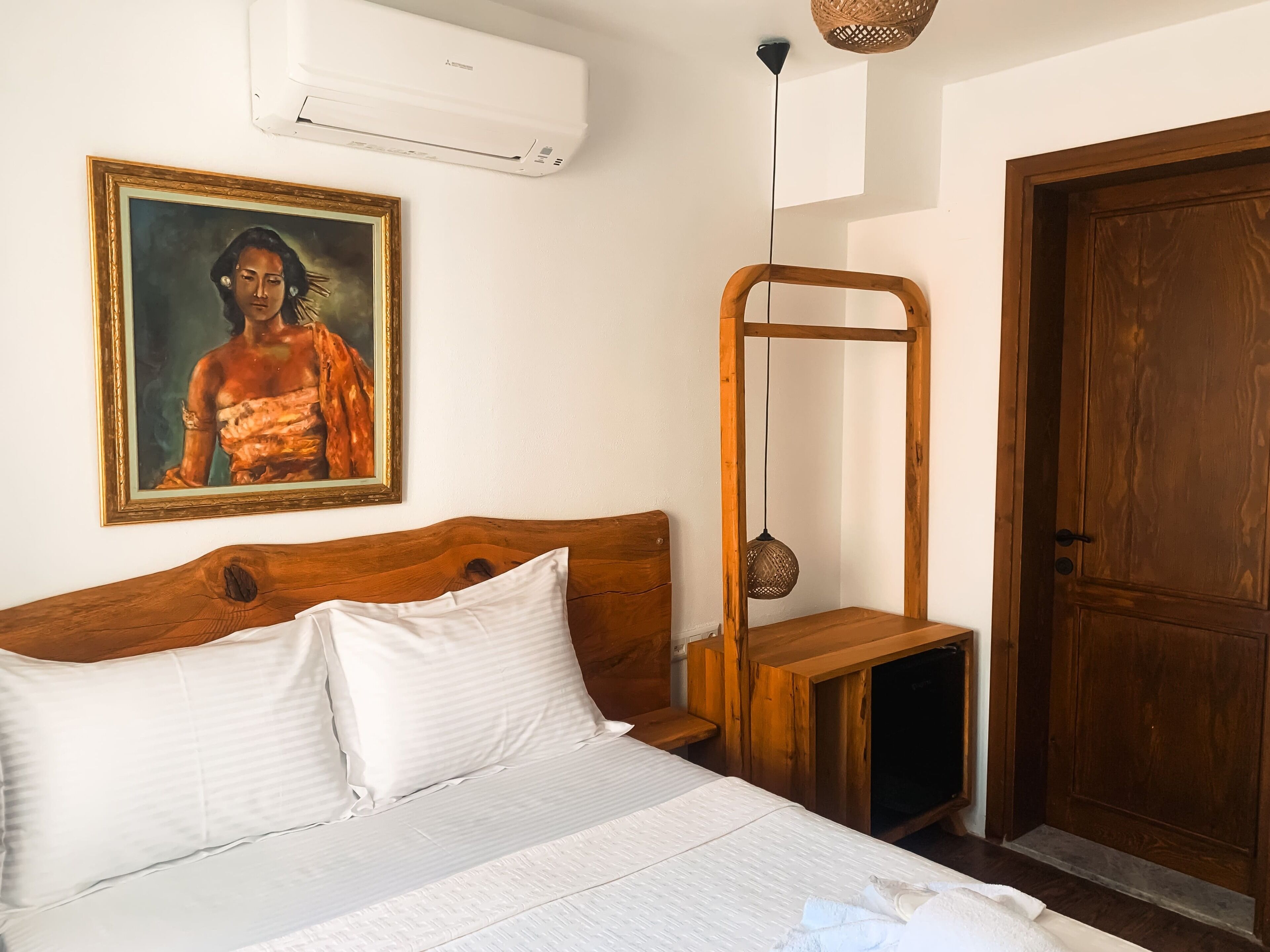 Un dormitorio con cama de madera, almohadas blancas, un cuadro, un armario de madera y una puerta.