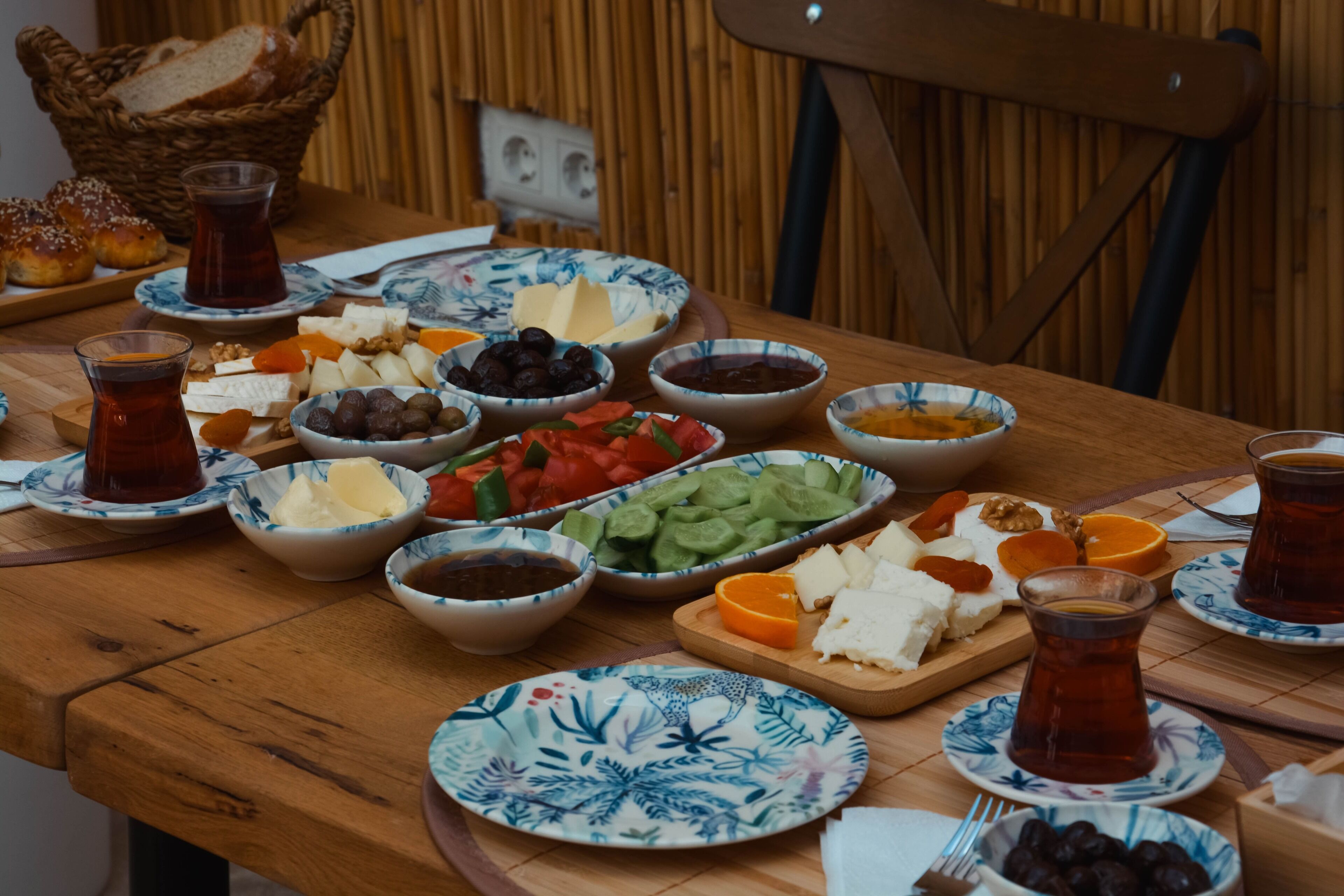A wooden table with various food items and drinks, including cheese, olives, and sliced vegetables.