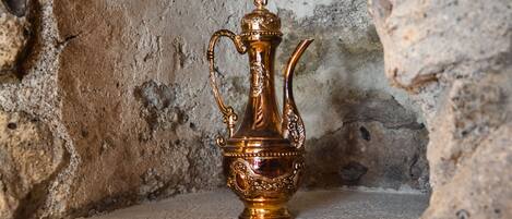 A brass teapot with a handle and spout, placed on a stone ledge against a textured stone wall.