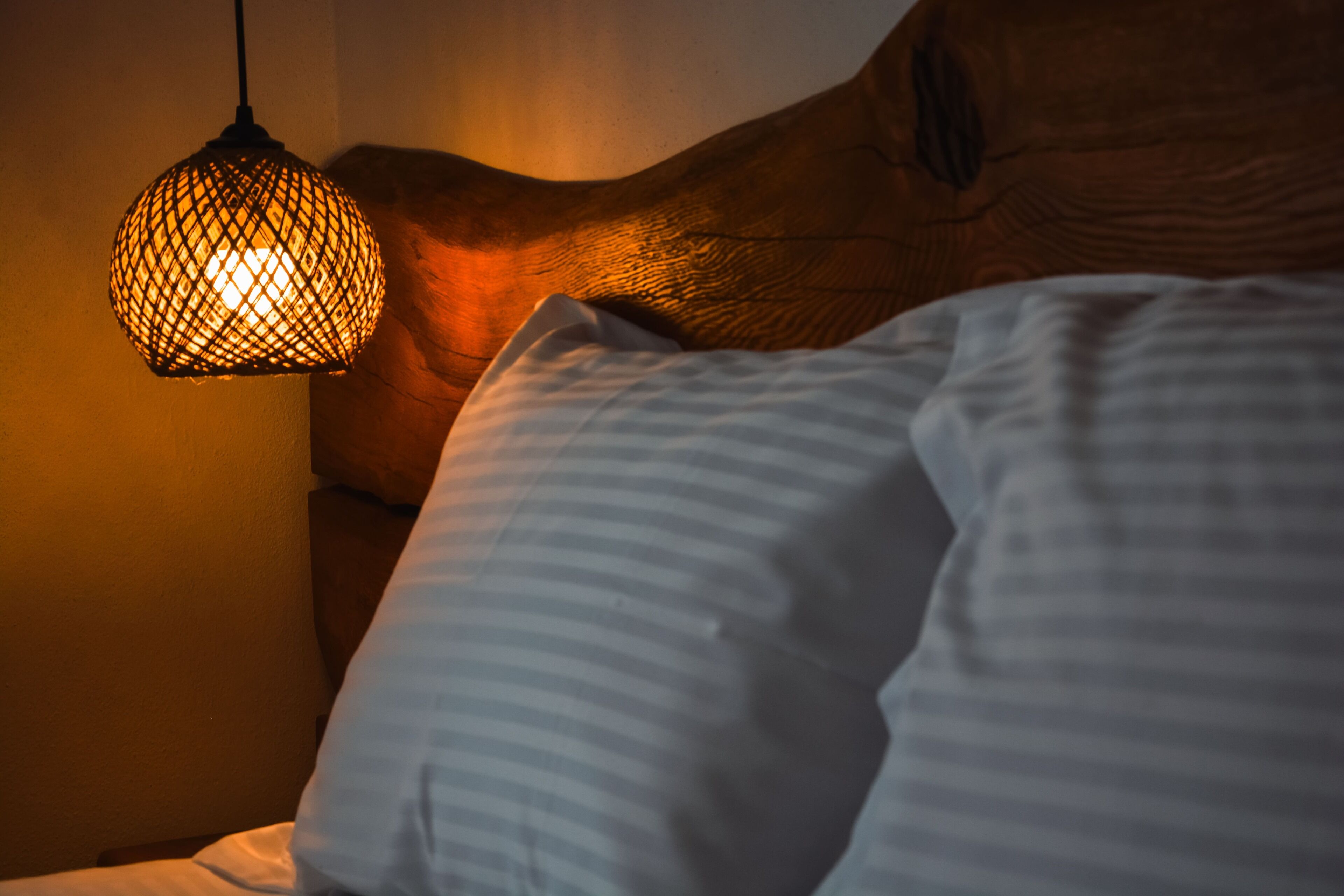 A close-up of a bed with a wooden headboard and a textured wall.