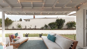 A covered outdoor seating area with two sofas, a small table, and string lights.