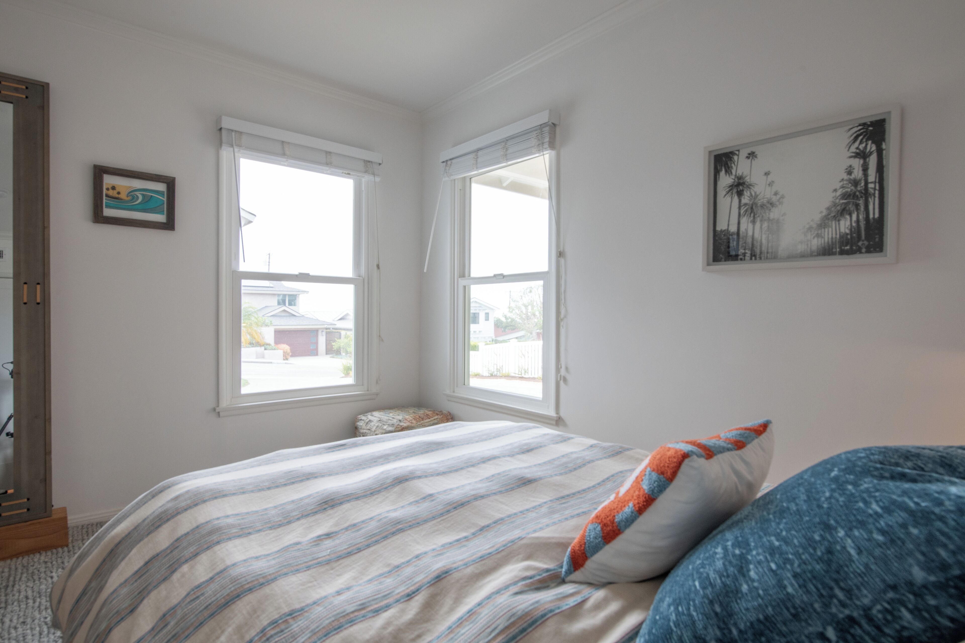 A bedroom with a bed, two windows, a framed picture, and a door.