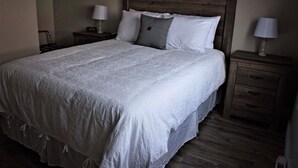 A large bed with a wooden headboard, two bedside tables with lamps, and a wooden floor. - Gros Morne Coastal Suites #2 (Rocky Harbour)