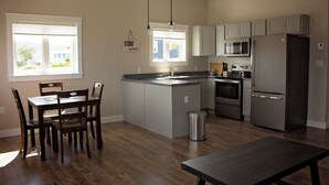 A modern kitchen with a central island, built-in appliances, and a dining area with wooden chairs. - Gros Morne Coastal Suites #2 (Rocky Harbour)