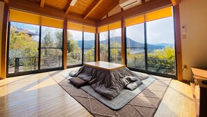 Une pièce dotée de grandes fenêtres, d’un plafond en bois et d’une table centrale entourée de coussins.