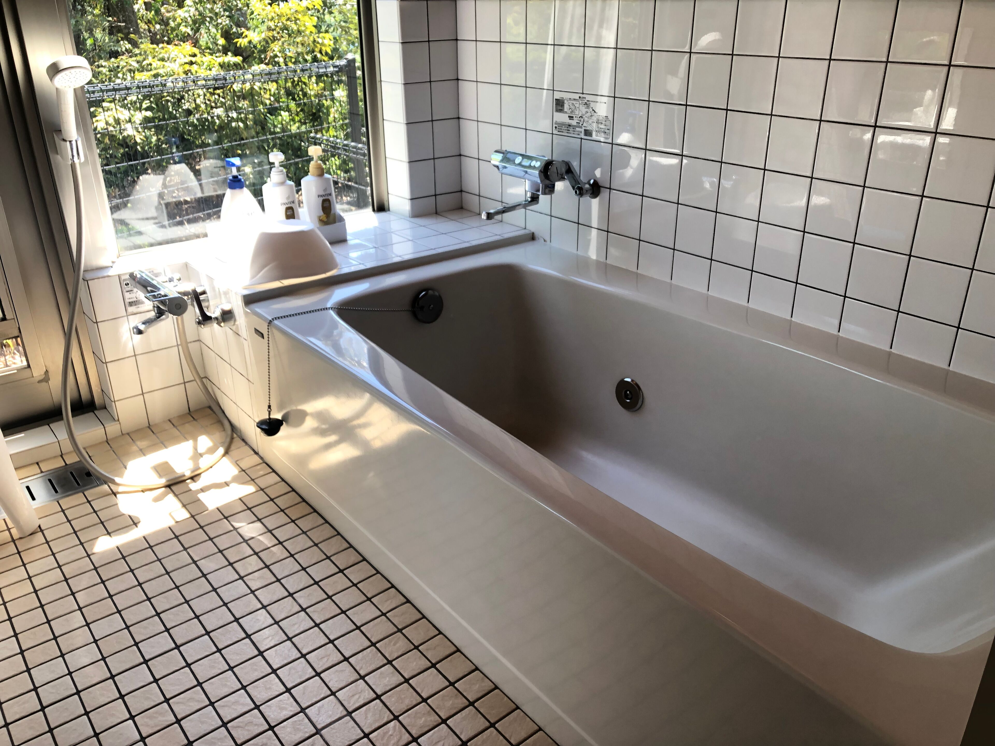 A modern bathroom with a large bathtub, a shower, and a window providing a view of greenery outside.