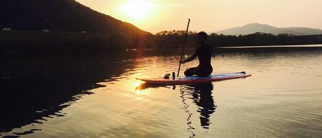 A person paddleboarding on a calm body of water during sunset.