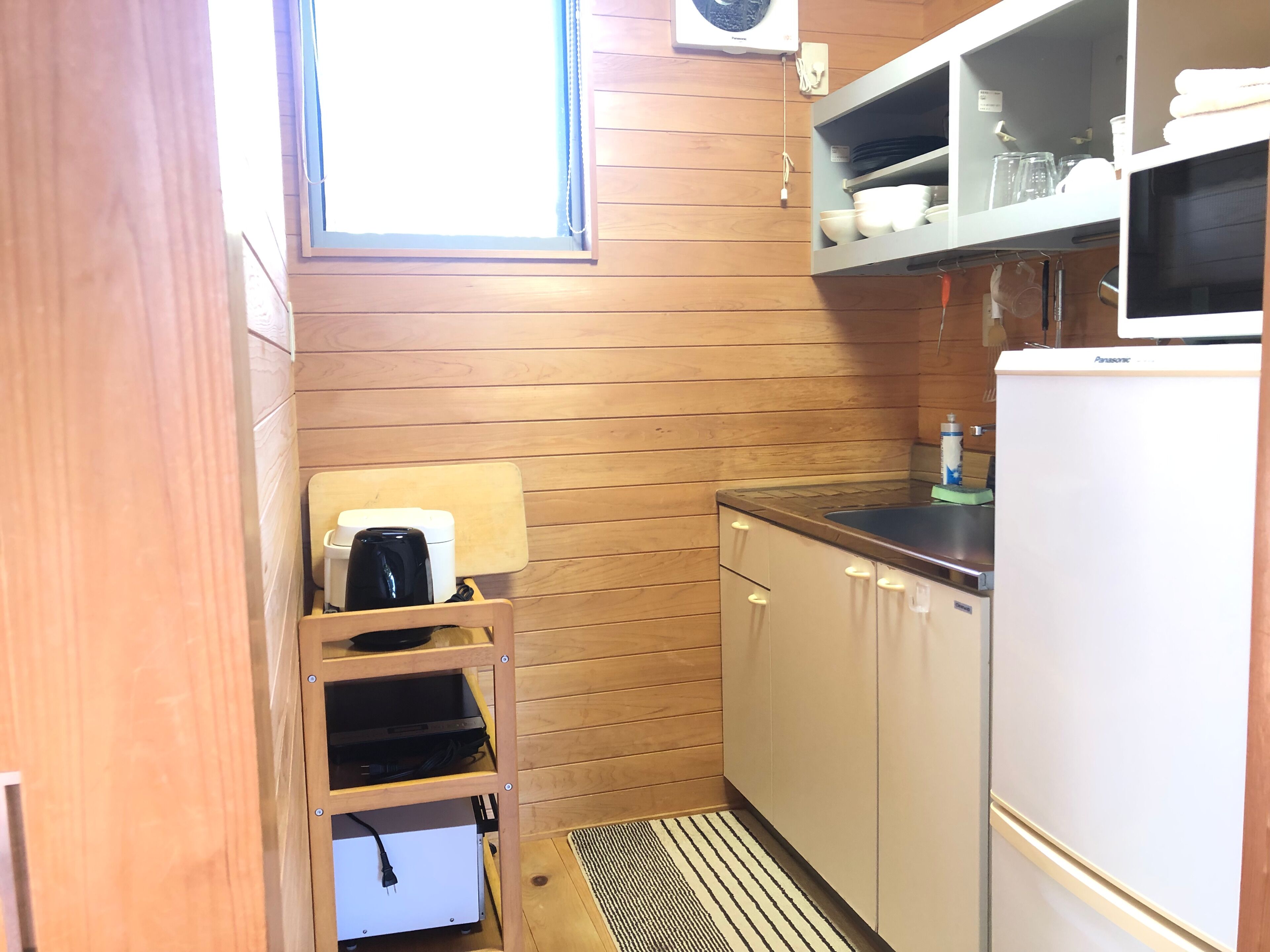A compact kitchen with wooden walls, a built-in sink, and a refrigerator.