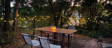 Ein Holztisch mit Stühlen im Freien, umgeben von einem Garten mit Bäumen und Lichterketten.
