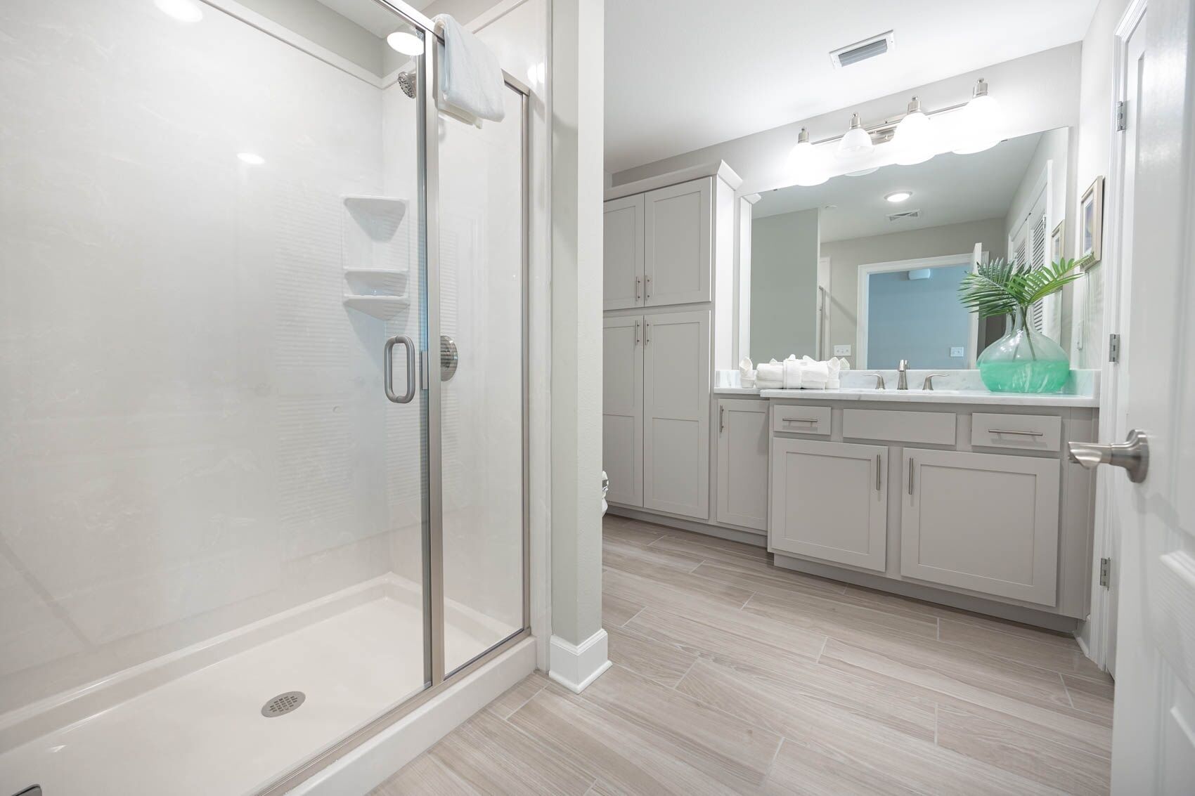 A modern bathroom with a glass-enclosed shower, white cabinetry, and a large mirror above the sink.
