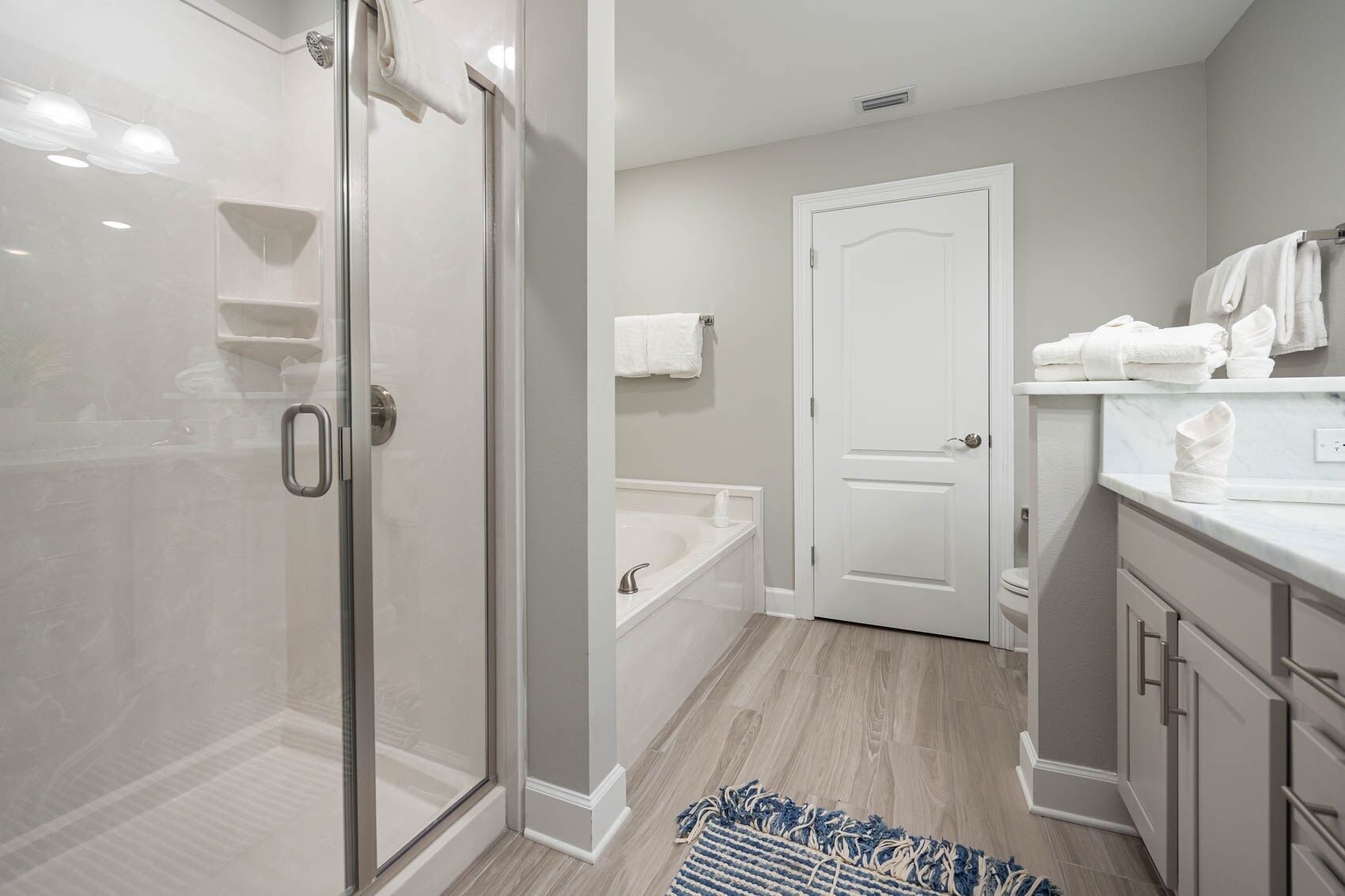 A modern bathroom with a glass shower enclosure, a bathtub, and a vanity with a towel rack.