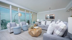 A spacious living room with a large window, a chandelier, and a view of the balcony. - Phoenix Gulf Towers 806 2 Bedroom Condo (Orange Beach)