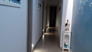 A hallway with a tiled floor, a white door on the left, and a wall with a blue mural. - Emme21  (Naples)