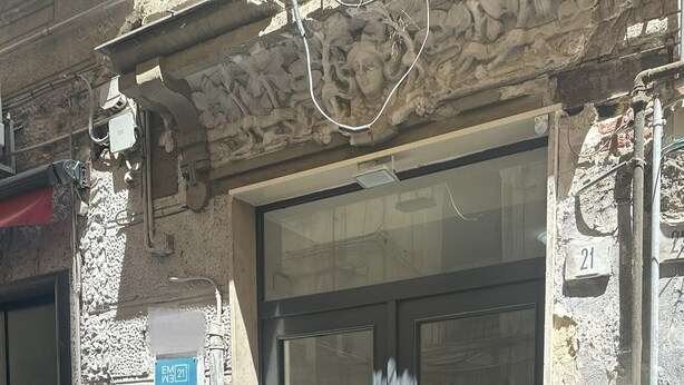 A building with a stone facade, a large glass door, and a blue emergency exit sign. - Emme21  (Naples)