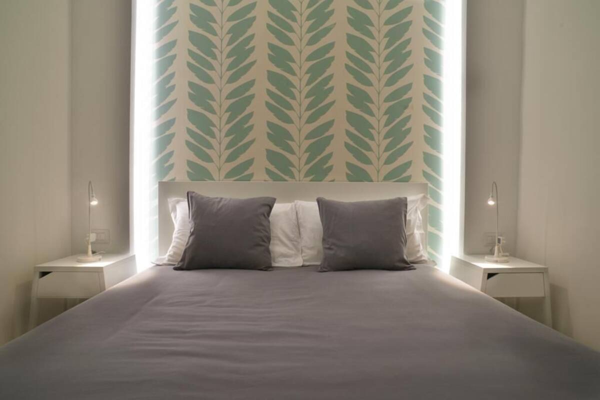 A modern bedroom with a large bed, two bedside tables, and a leaf-patterned wall.