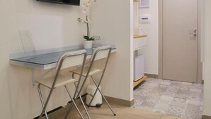 A small office space with a desk, two chairs, a potted orchid, a flat-screen TV, a door, and a tiled floor. - Emme21  (Naples)