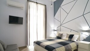 A modern bedroom with a large bed, a TV mounted on the wall, and a geometric wall design. - Emme21  (Naples)