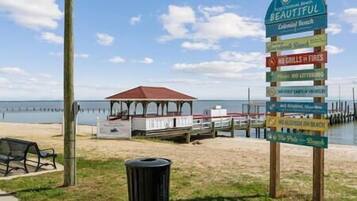 A beach sign with multiple directional arrows and text, a gazebo, and a pier extending into the water.