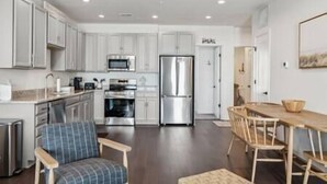 A modern kitchen with white cabinets, stainless steel appliances, and a dining area with a wooden table and chairs. - Sail Away To (Colonial Beach)