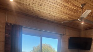 Een slaapkamer met een groot bed, een plafondventilator, een aan de muur bevestigde televisie en een schuifdeur naar een buitenruimte.