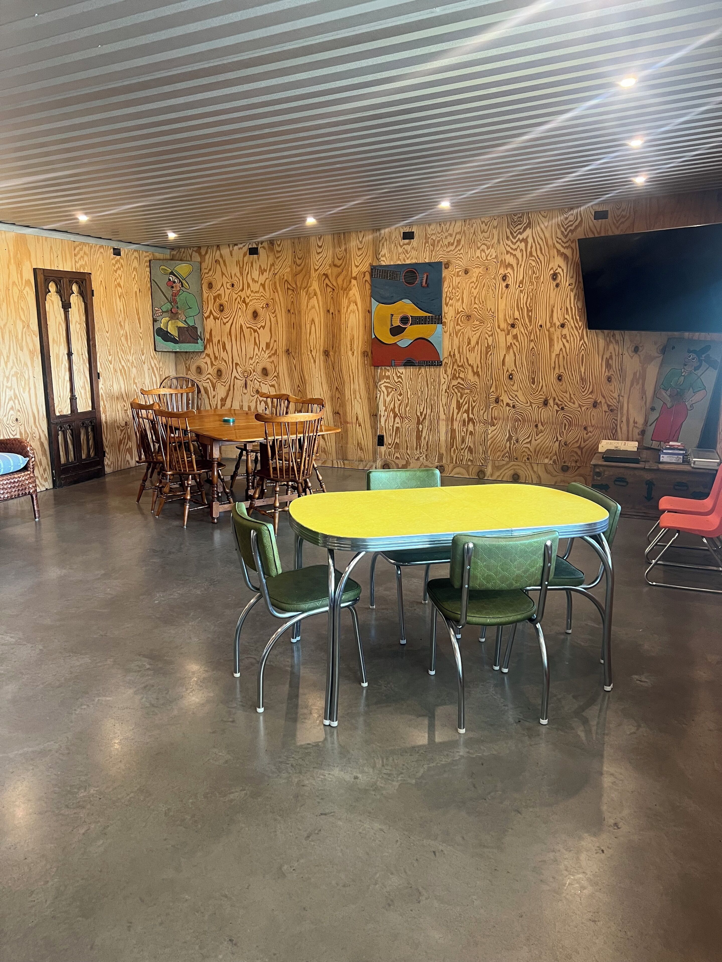 A conference room with a wooden wall, a round table with green chairs, and a flat-screen TV on the wall.