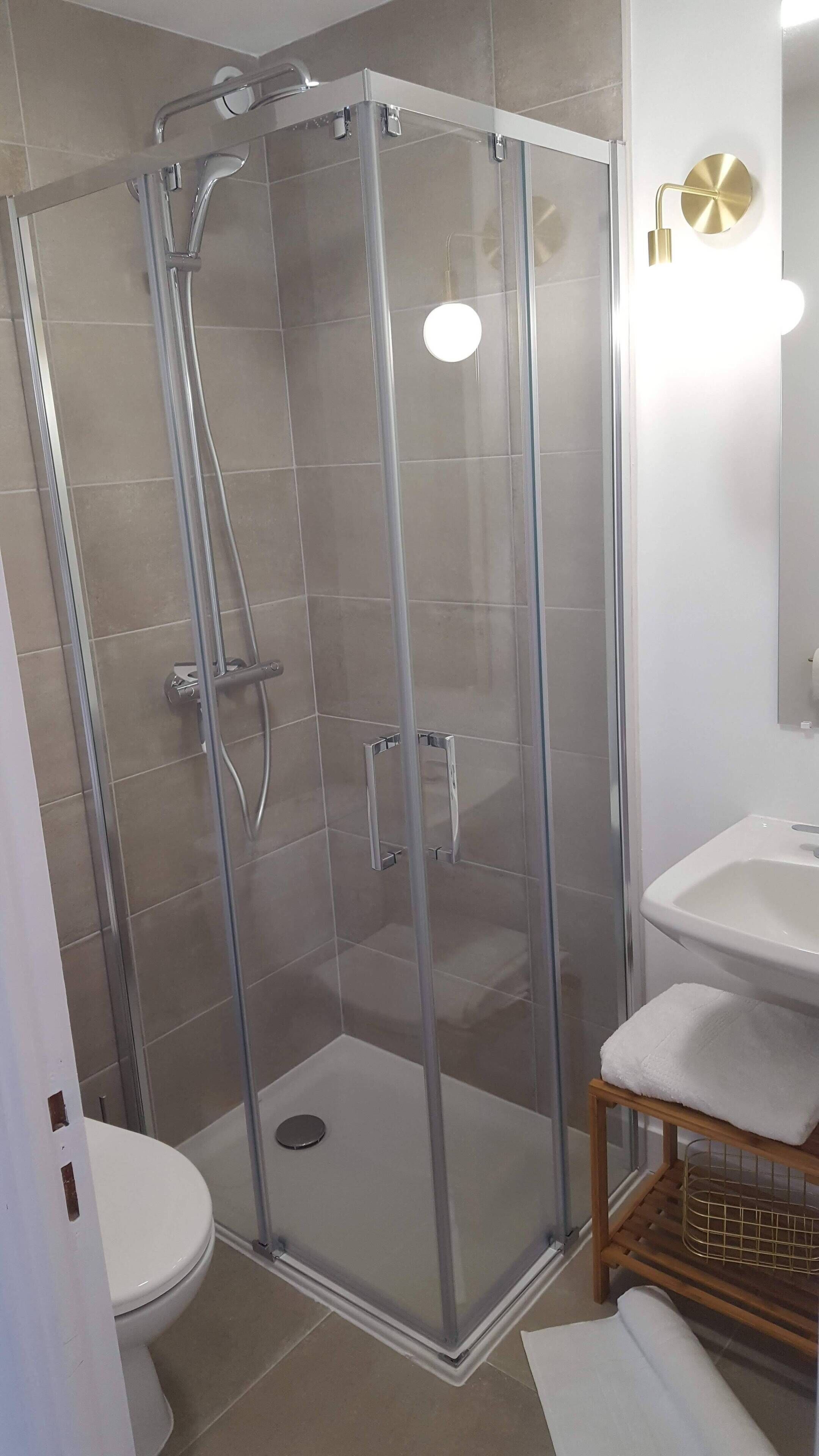 Et bruseafsnit med glasdør, toilet og vask med håndklæde.