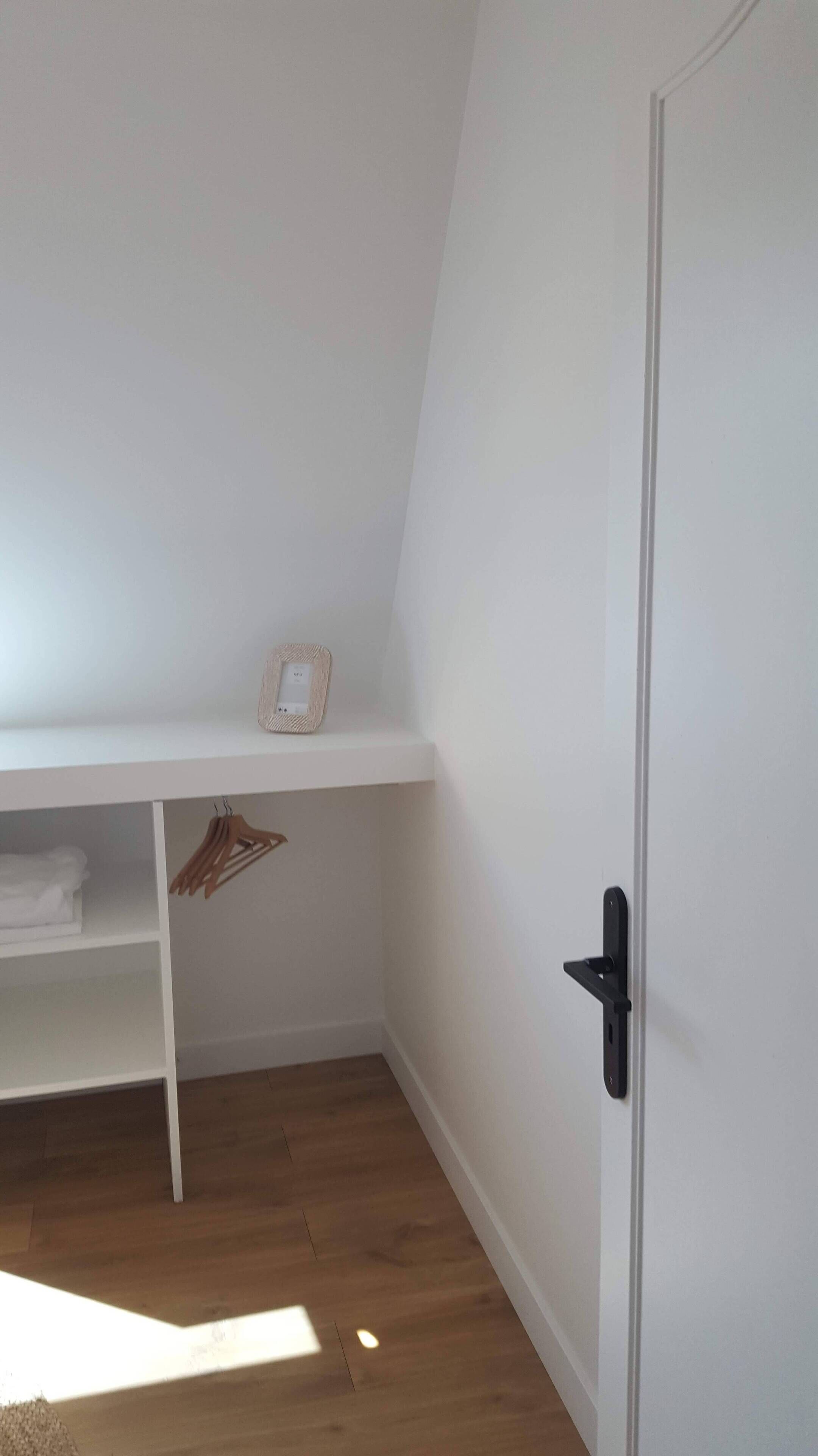 Ein Zimmer mit einer weißen Tür, einem weißen Regal mit einem Korb und Holzboden.
