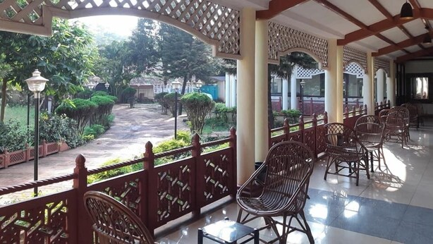 A covered outdoor area with wicker chairs and a pathway leading to a garden. - Empires Joda  (Barbil)