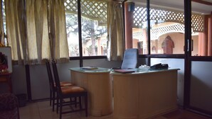 A room with a desk, two chairs, a window with curtains, and a view of an outdoor area with a tree and a building. - Empires Joda  (Barbil)