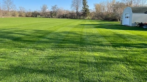 A well-maintained grassy field with a white barn and a shed in the background. - Lake Ontario getaway 30 mins from Alexandria Bay and the famous Bolt Castle. (Dexter)