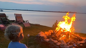A child sitting on a wooden bench overlooking a campfire by a lakeside. - Lake Ontario getaway 30 mins from Alexandria Bay and the famous Bolt Castle. (Dexter)