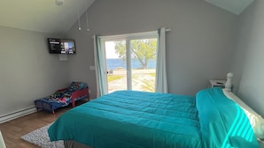 A bedroom with a large bed, a television on the wall, and a view of the outdoors. - Lake Ontario getaway 30 mins from Alexandria Bay and the famous Bolt Castle. (Dexter)