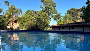 Une piscine d’un bleu éclatant, bordée d’une structure en pierre, et en arrière-plan, un bâtiment avec un toit recouvert de tuiles.