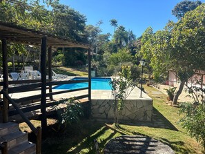A backyard with a swimming pool, a wooden pergola, and a stone wall. - Pousada Recanto Guará (Pirenópolis)