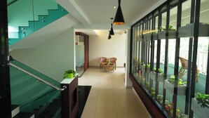 Un interior moderno con una escalera de cristal, una zona de comedor con mobiliario de mimbre y plantas en macetas.