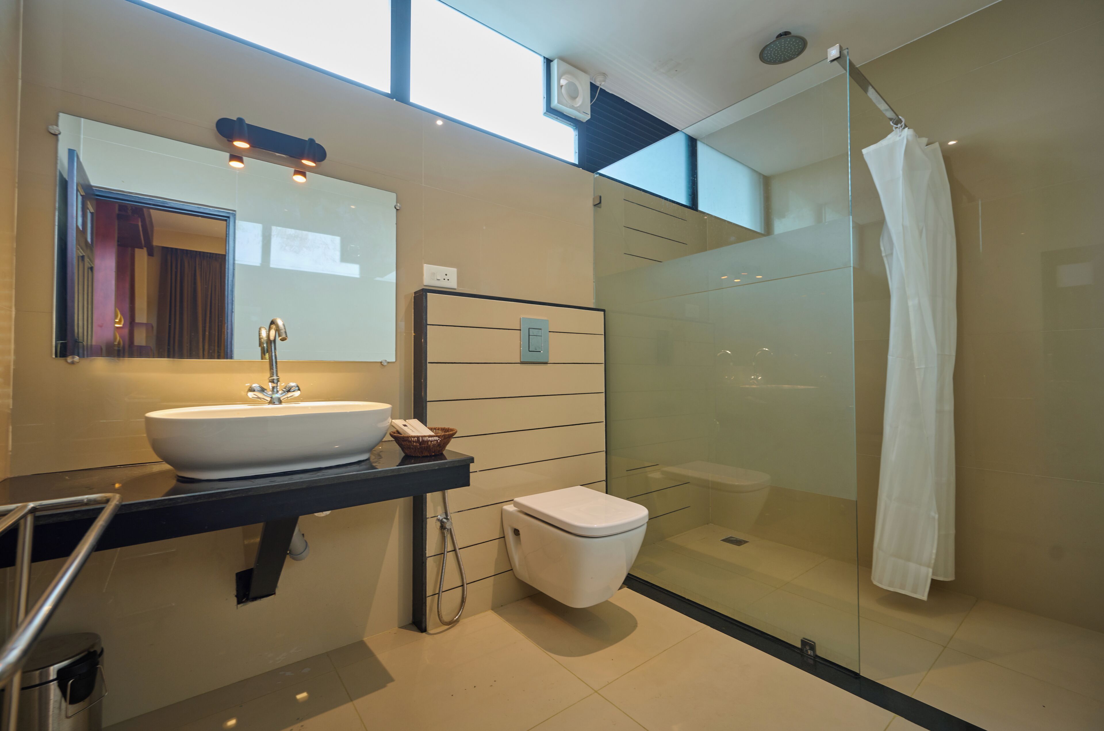 Un baño moderno con ducha de vidrio, un lavamanos con espejo y un inodoro.