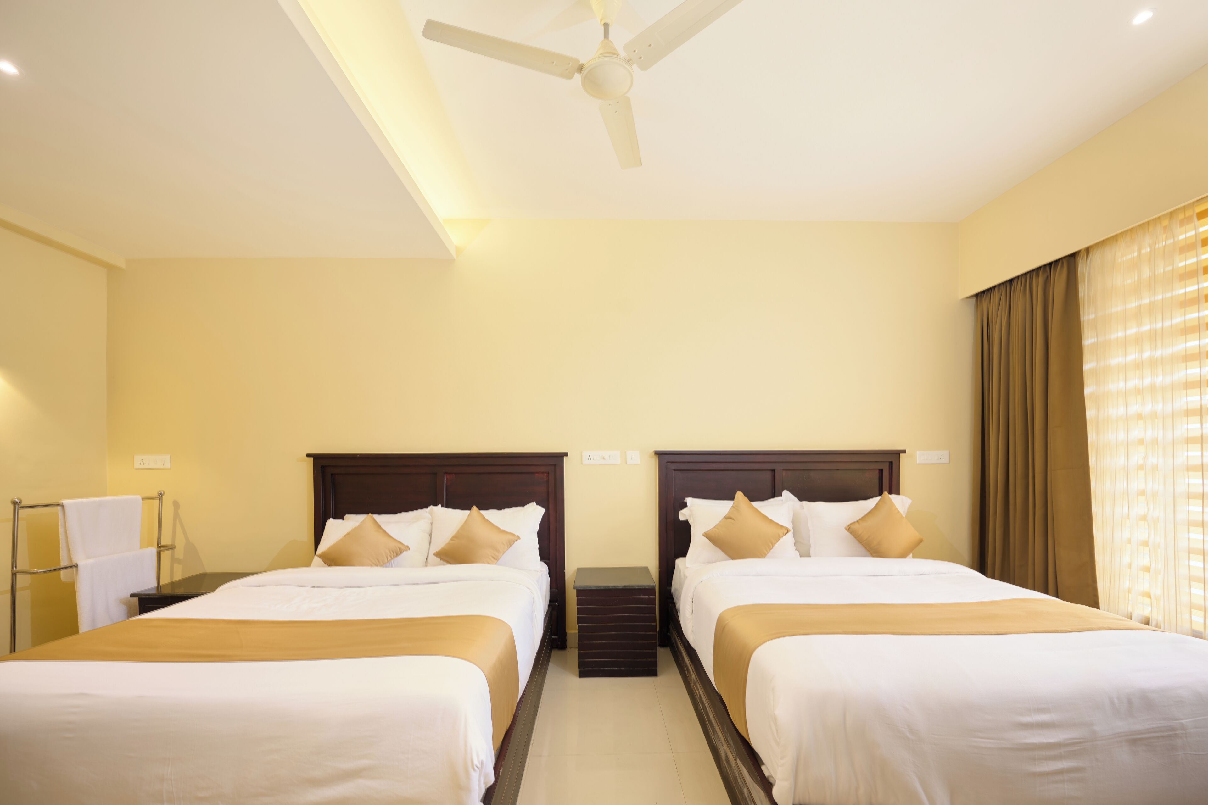A hotel room with two beds, a ceiling fan, and a window with curtains.