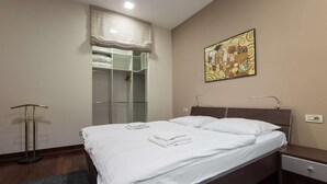 Un lit bien fait, avec du linge de lit blanc, une table de chevet, une commode, une armoire avec un miroir et un tableau accroché au mur.