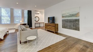 A modern living room with a sofa, a coffee table, and a TV. There are large windows, a painting on the wall, and a wooden cabinet. - Welcome to “Chateau Sherbrooke's” loft: an historic gem in Downtown Montreal. (Montréal)