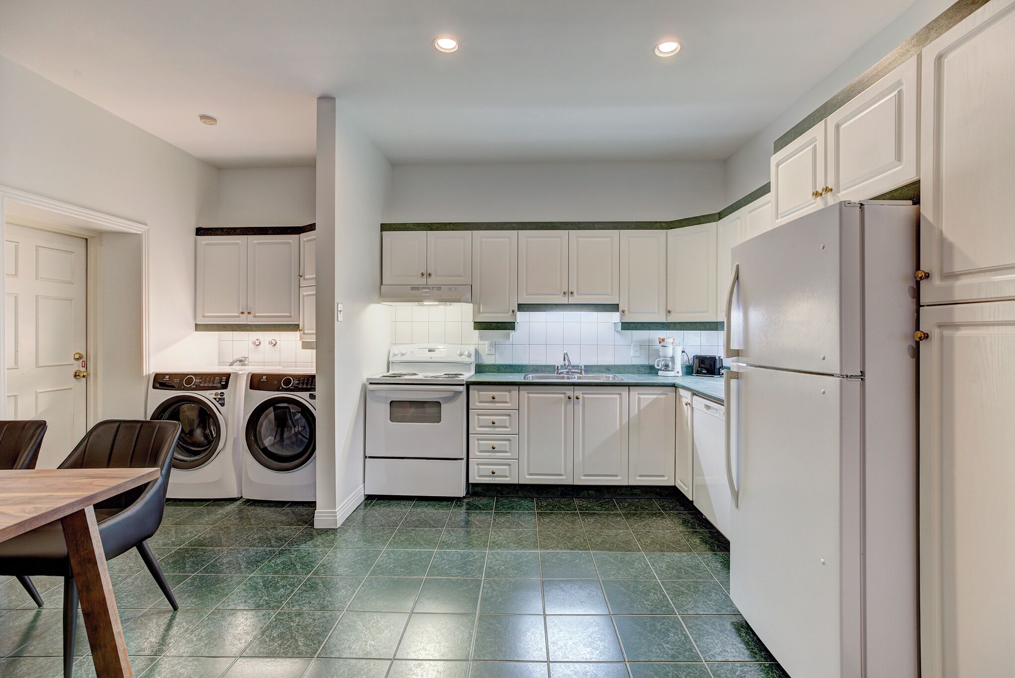 A compact kitchen with white cabinets, a built-in oven, a washing machine, and a refrigerator.