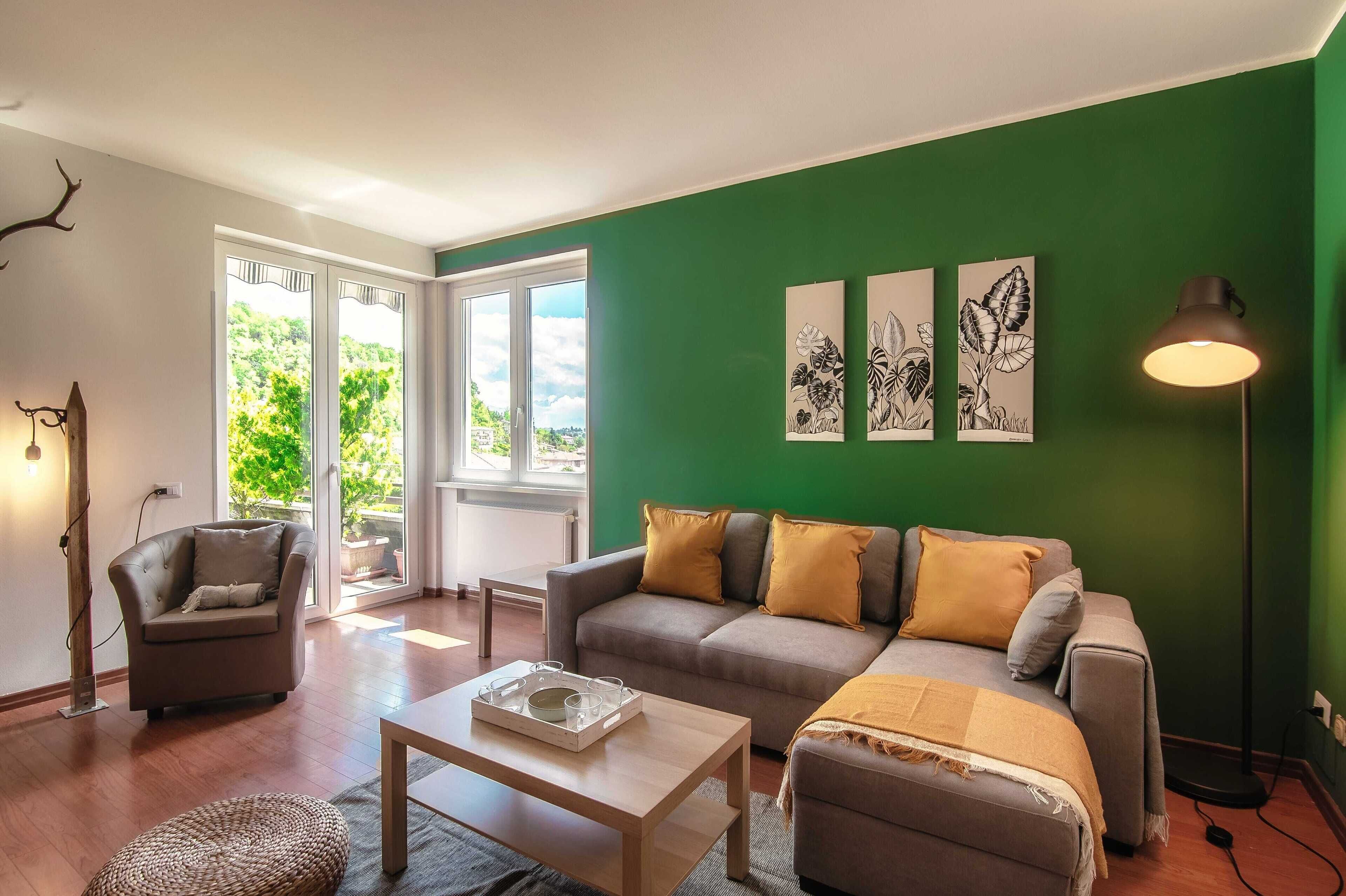 A living room with a green wall, a grey sofa, a wooden coffee table, and a floor lamp.