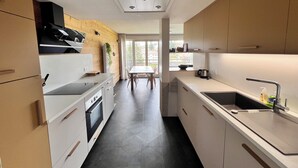 A modern kitchen with white cabinets, a black stove, and a window overlooking a balcony. - Mountain apartment with a beautiful view on the village of Les Rousses (Les Rousses)