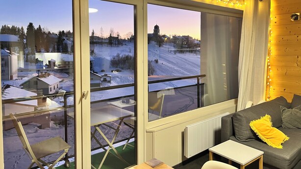A room with a view of a snowy landscape, a balcony with a chair, and a couch with a yellow pillow. - Mountain apartment with a beautiful view on the village of Les Rousses (Les Rousses)