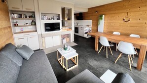 A modern living room with a sofa, a TV, and a dining area with chairs and a table. - Mountain apartment with a beautiful view on the village of Les Rousses (Les Rousses)