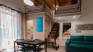 Ein modernes Wohnzimmer mit Essbereich, einem blaugrünen Sofa, einer Treppe und einem großen Fenster mit transparenten Vorhängen.